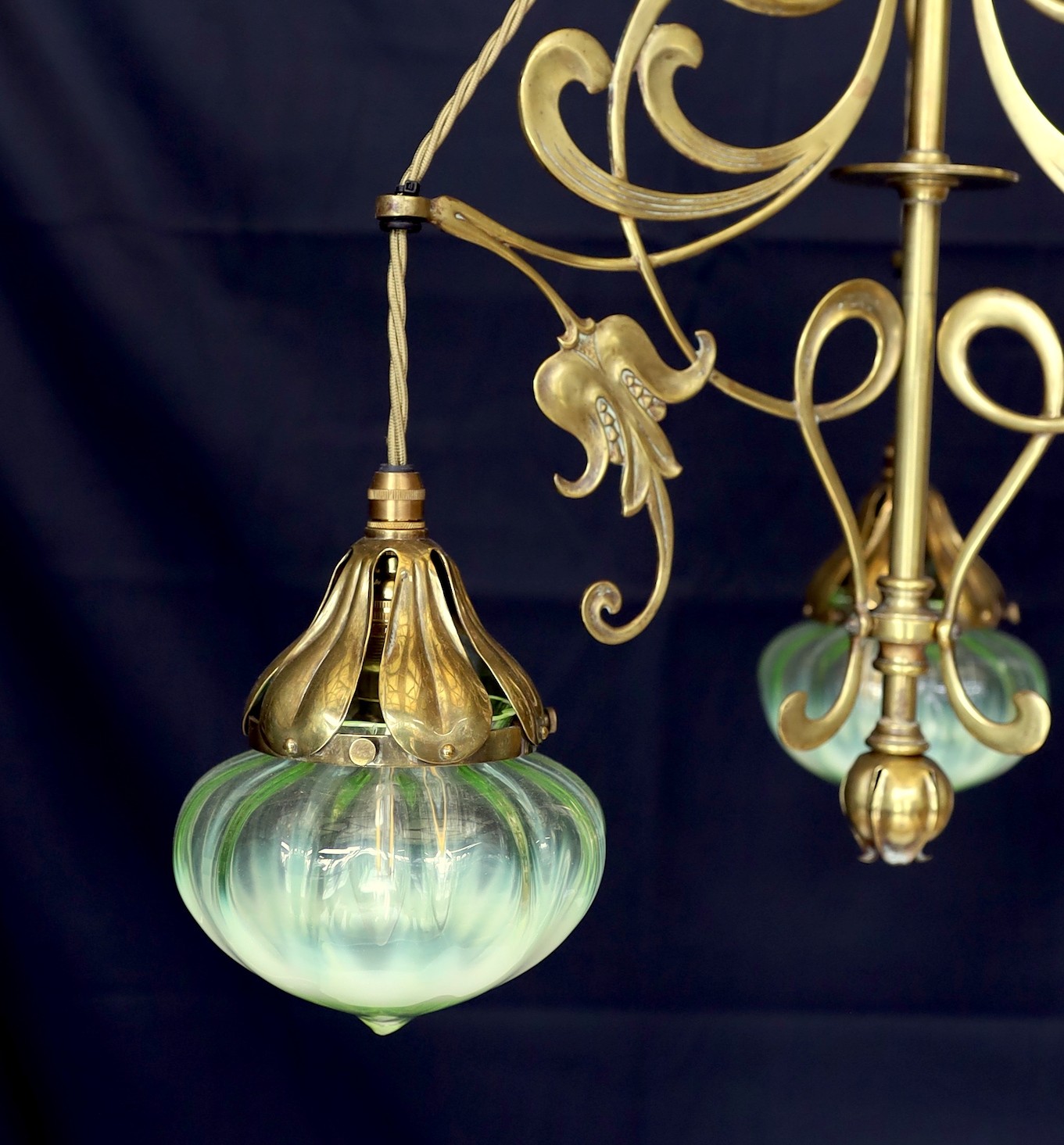 An English Arts & Crafts brass light fitting with scrolling foliate branches and tinted iridescent glass shades, height 68cm. width 46cm